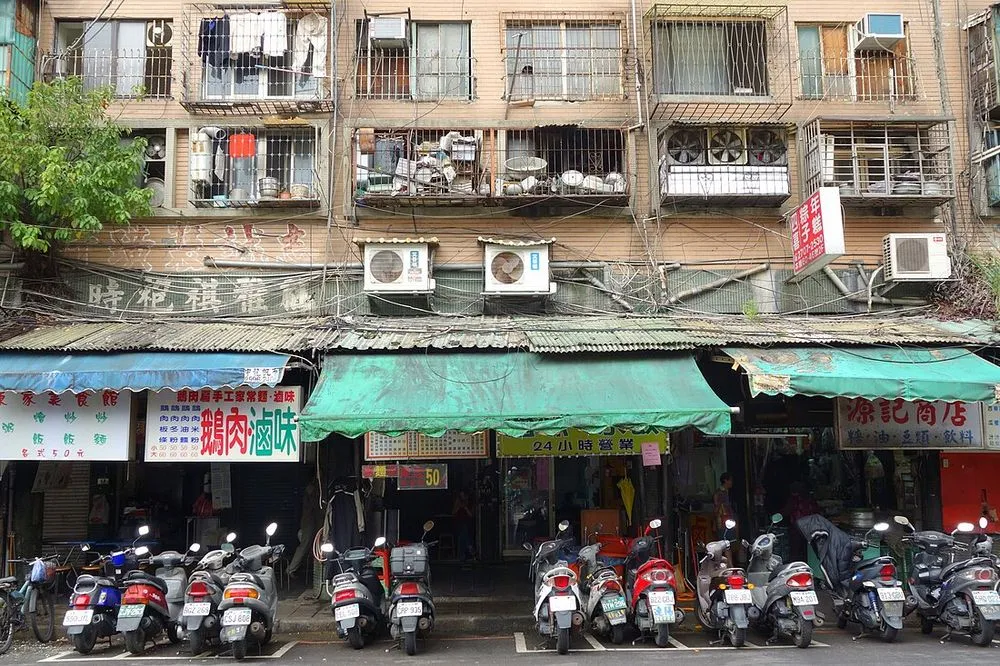 台北市大安路一棟舊公寓的外牆，牆面上掛著多台冷氣室外機，並有鐵窗與招牌。